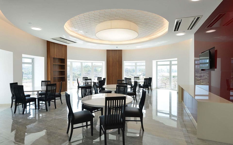 Round dining tables under a circular coffered ceiling with a honeycomb-patterned recess and drum pendant