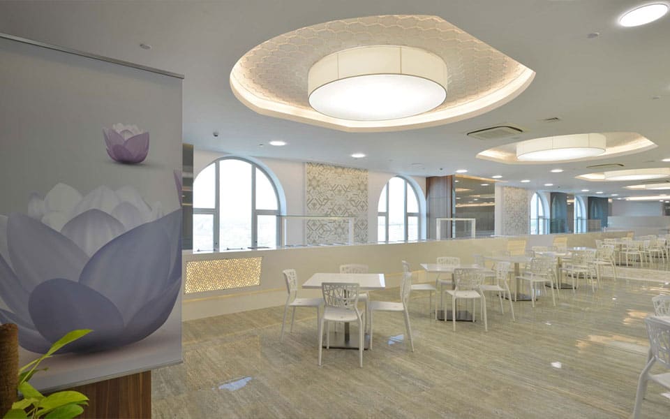 Canteen hall with white moulded chairs under circular ceiling coffers and arched perimeter windows