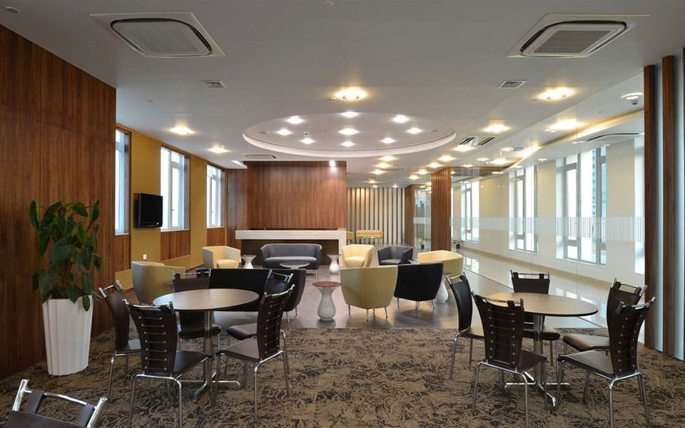 Breakout lounge with mustard and grey tub chairs on patterned carpet against full-height walnut panelling