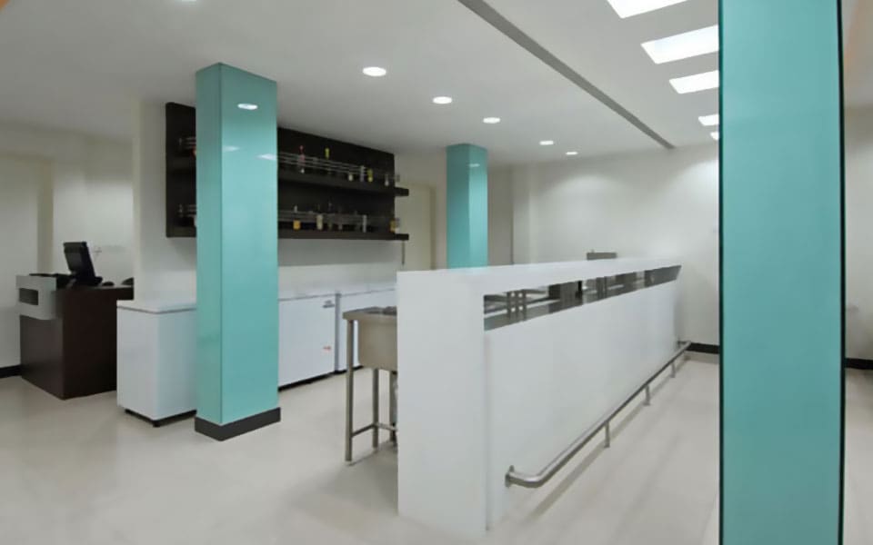 Servery counter in white solid surface with inset steel wells and a footrail, beside aqua clad columns