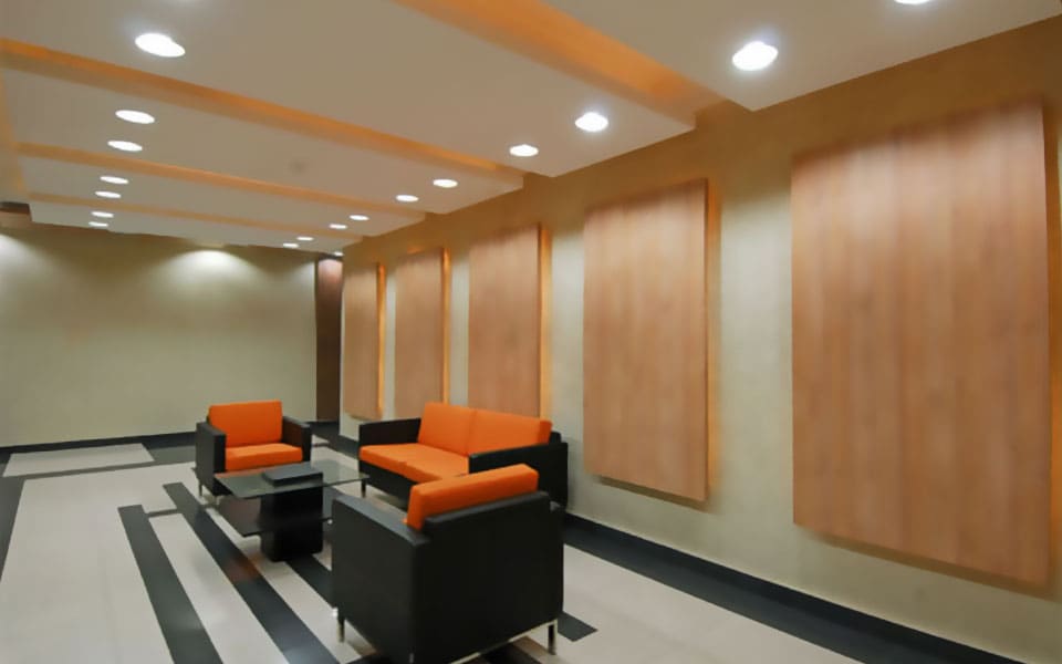 Corridor lounge with lit timber veneer wall panels, orange cushioned seating and dark inlay bands in ivory tiling