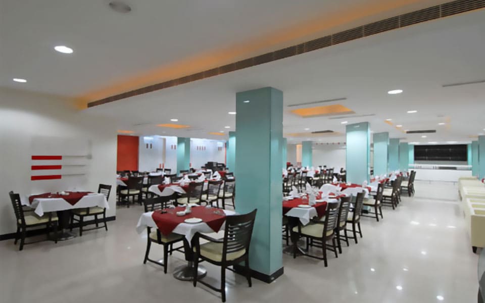 Dining hall with maroon-clothed tables and slat-back chairs between aqua clad columns under a slatted timber band
