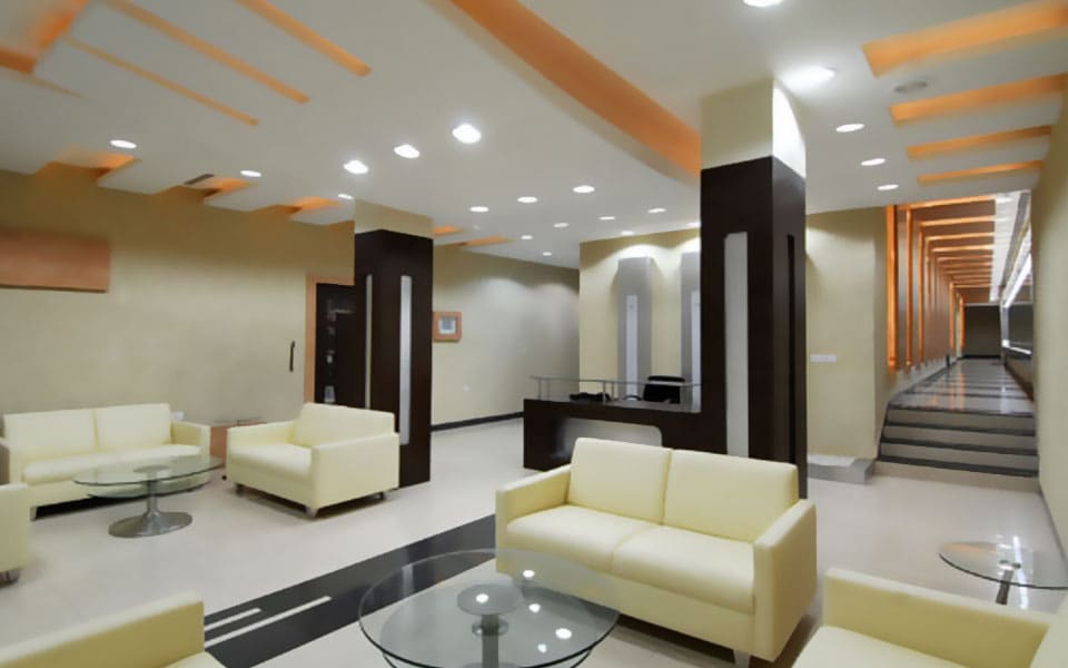 Club lobby with cream sofas and glass tables, a veneer host desk, and a stair beside a warmly lit portal corridor