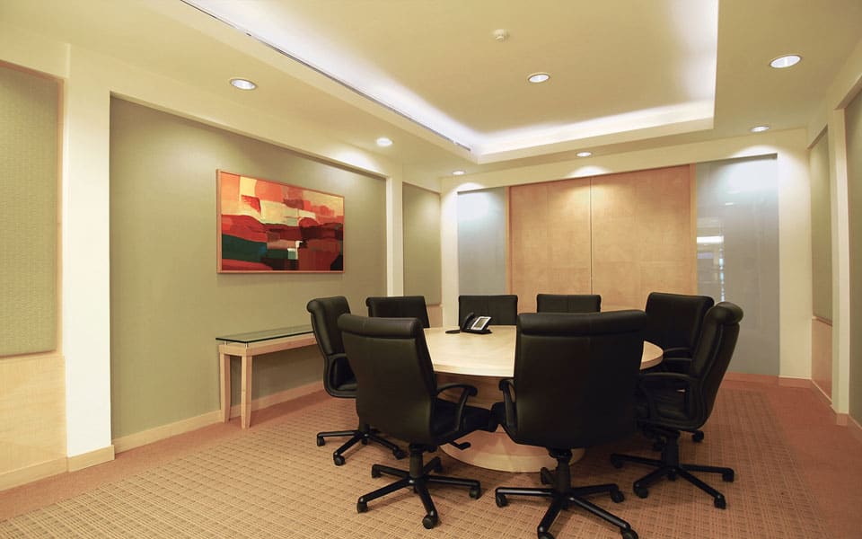 Boardroom with an oval maple table, black leather chairs and sage fabric wall panels under a cove-lit ceiling tray