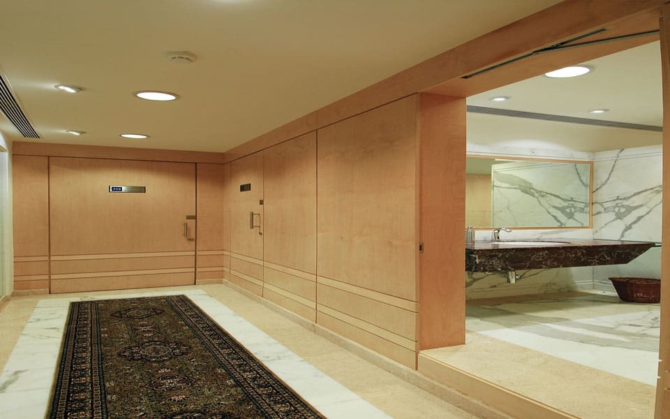 Veneer-panelled vestibule with a patterned rug runner, opening to a washroom clad in white marble with a stone vanity