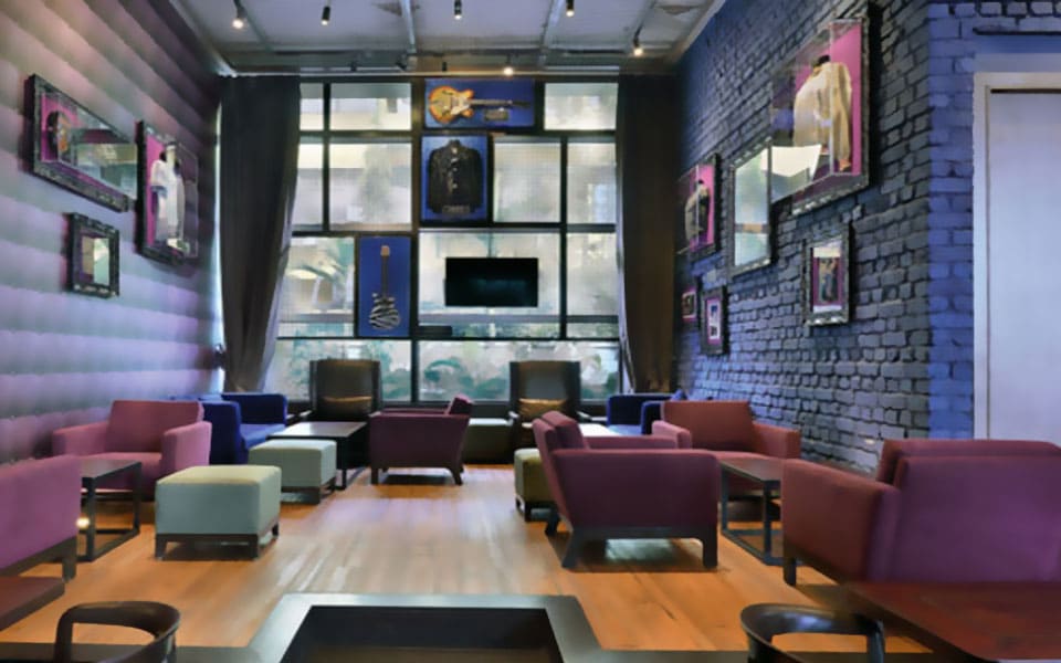 Lounge chairs and ottomans between a tufted purple wall and painted brick hung with memorabilia