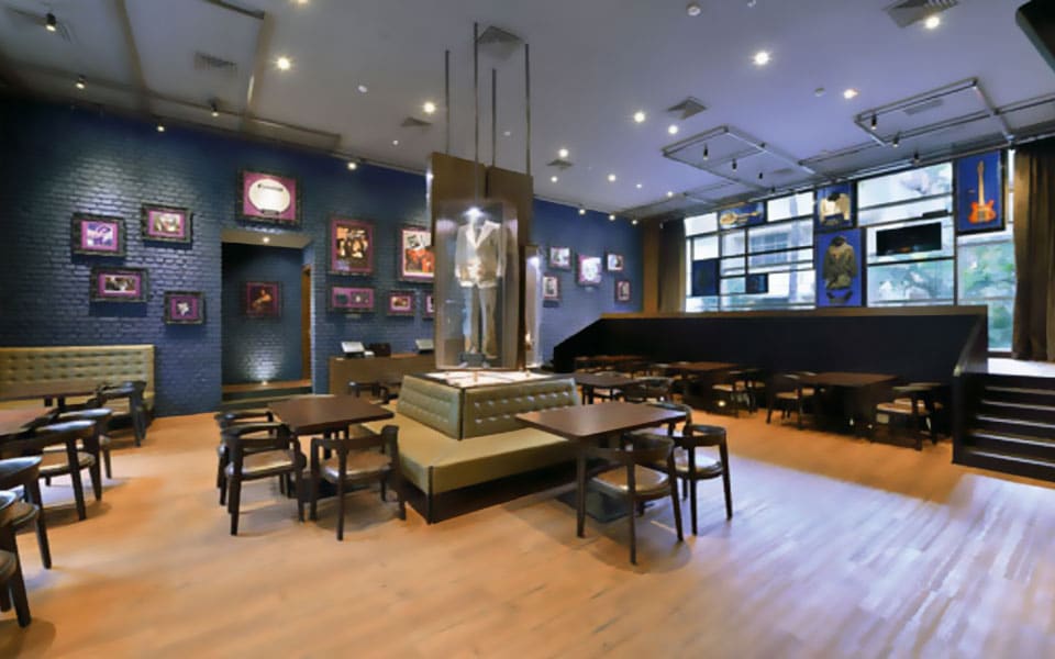 Dining floor against navy painted brick, with a lit display vitrine and olive tufted banquettes