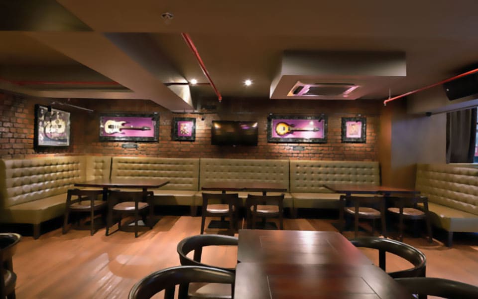 Banquette seating in cream tufted upholstery below framed guitars on exposed brick, with red pipework