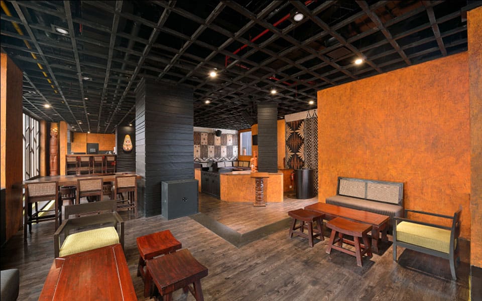 Cane-back settees and low timber tables against a rust-orange wall, facing a raised service counter