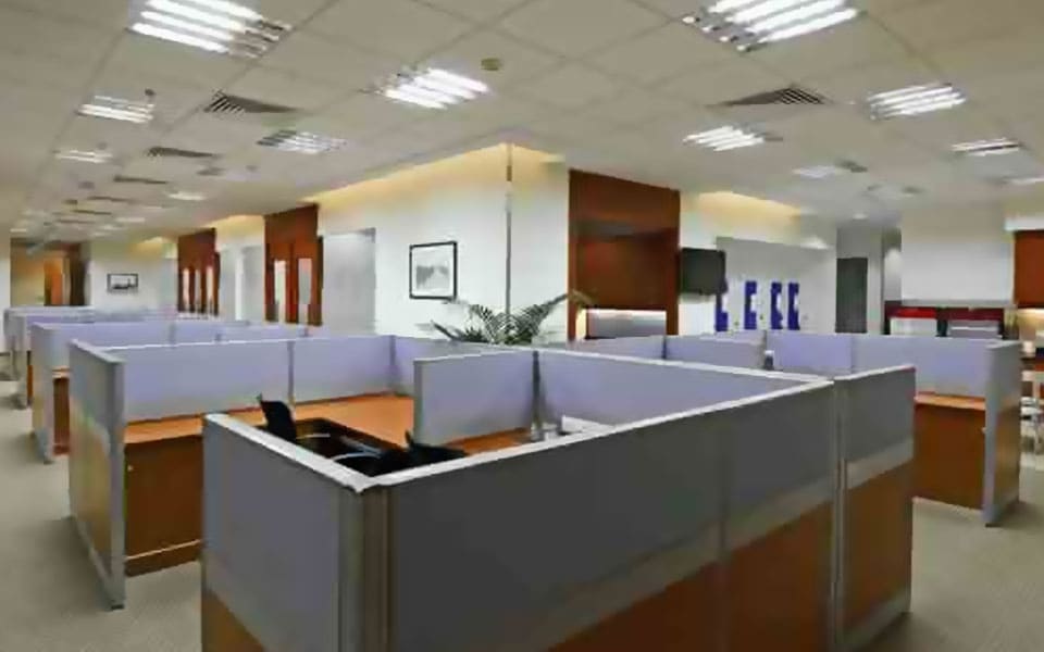 Open-plan floor of modular workstations with grey fabric screens and oak laminate tops under a mineral fibre grid ceiling