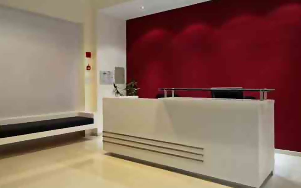 White reception counter with a grooved front and glass transaction top against a deep crimson feature wall