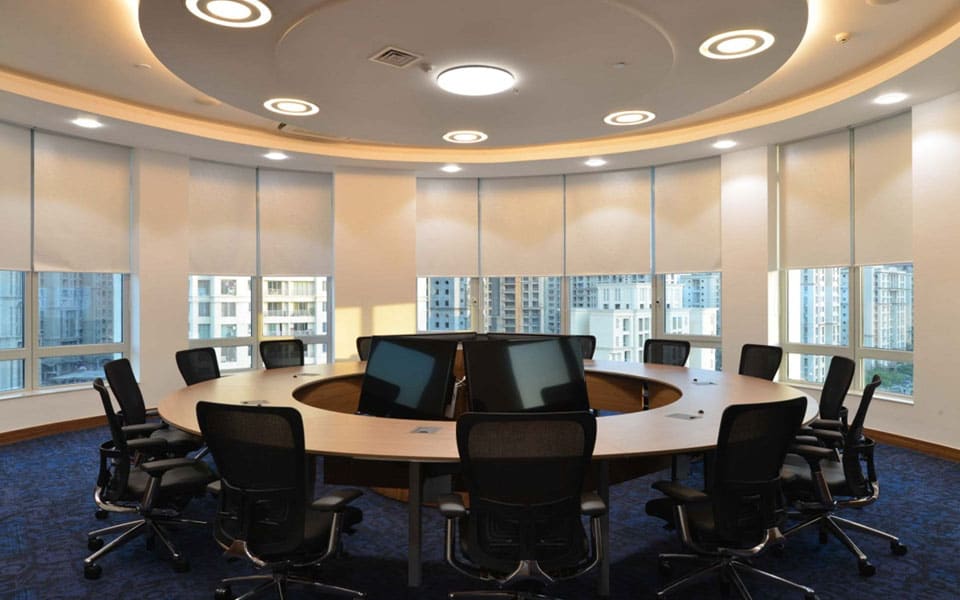 Circular boardroom with a doughnut-shaped veneer table, retractable monitors and concentric cove-lit ceiling rings