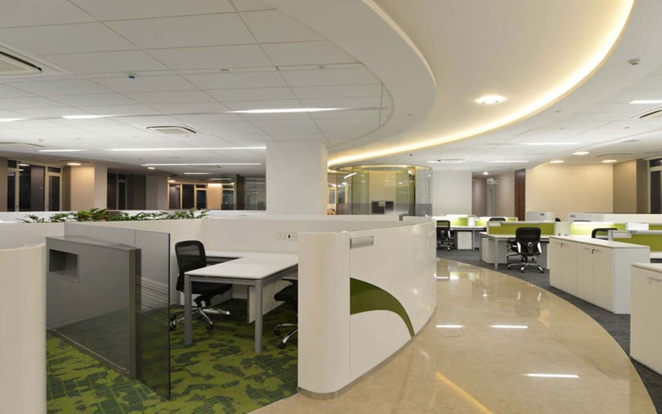 Open-plan floor with curved white workstation pods, green carpet tile inserts and a sweeping cove-lit ceiling curve