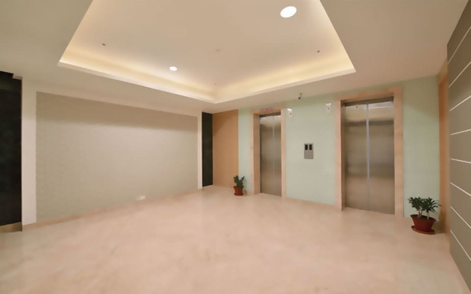 Lift lobby with two stainless steel lift doors in stone surrounds, a beige feature wall and a cove-lit ceiling tray