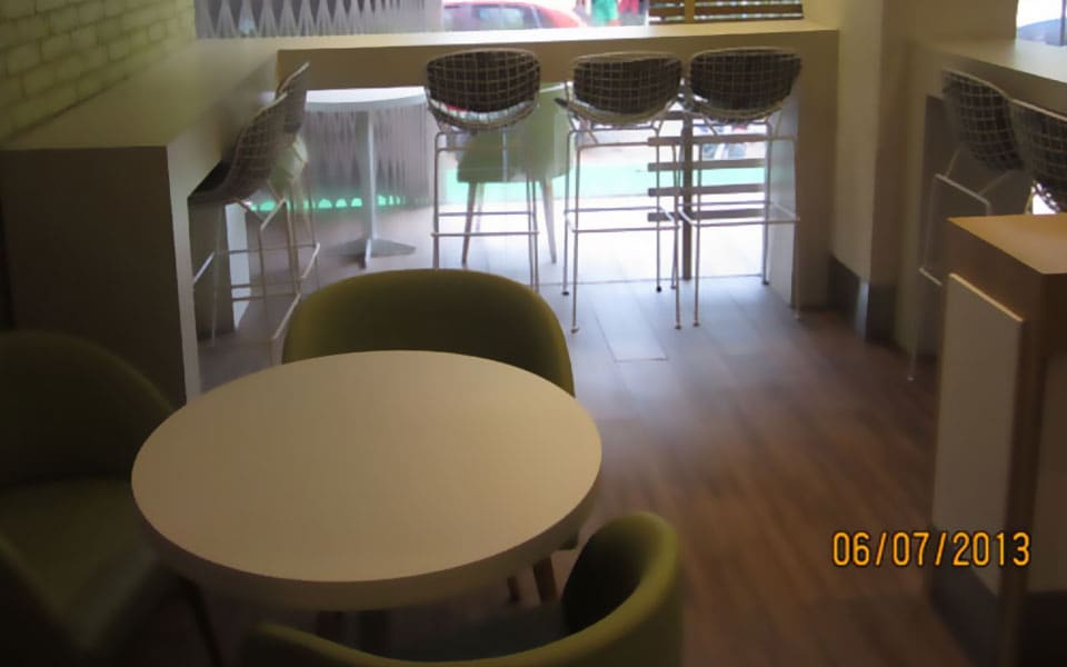 Seating area with a round white table, olive tub chairs and wire bar stools at a window counter