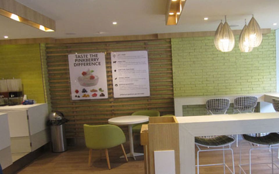 Seating area with green-washed brick, timber batten walls, olive tub chairs and woven pendant shades