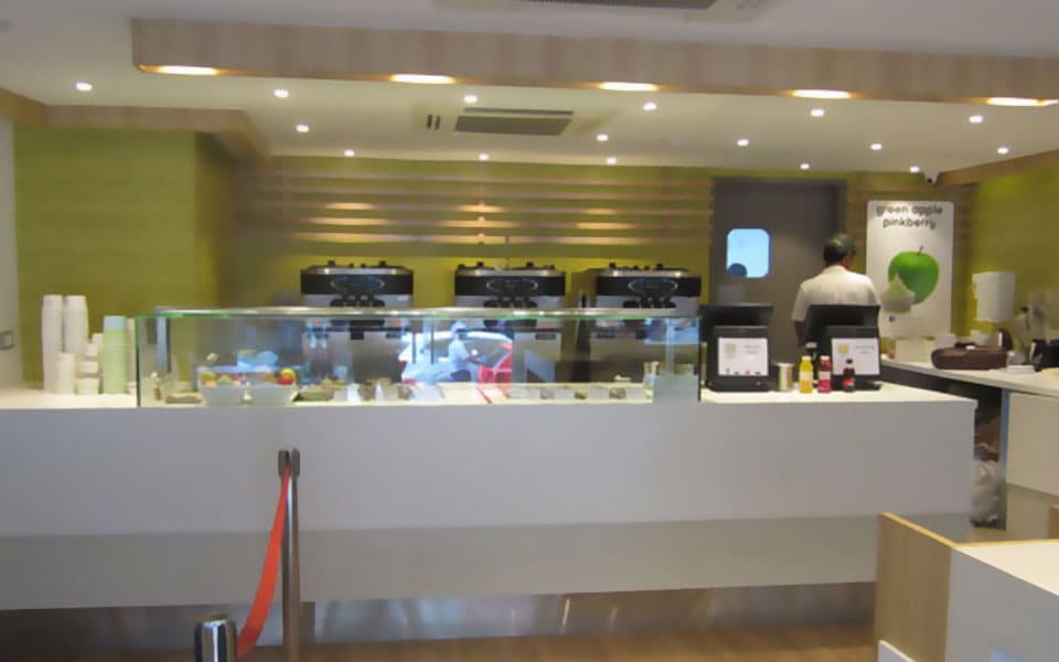 Full-width service counter under a slatted timber bulkhead, with soft-serve machines and topping display