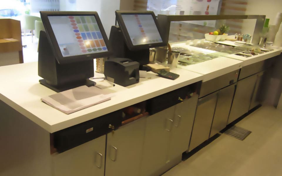 Service counter in white solid surface with two POS terminals and a stainless chilled topping well