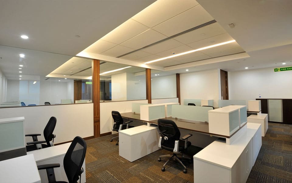 Open-plan workstations with timber tops and white storage under a stepped ceiling raft with cove lighting
