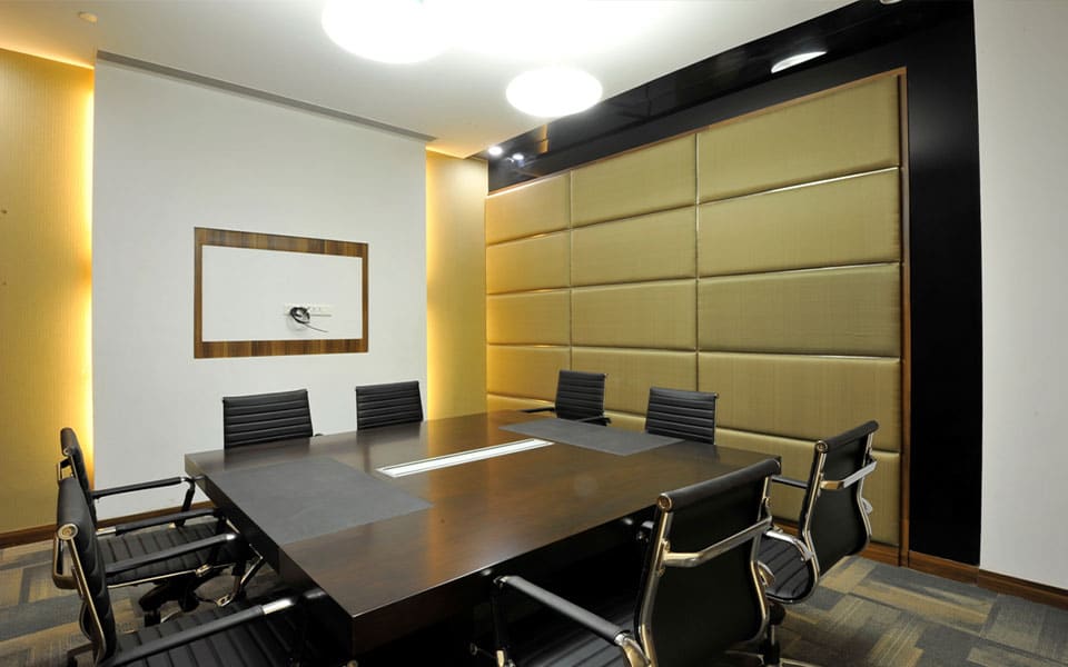 Meeting room with a wenge table, black leather chairs and a gold upholstered padded feature wall