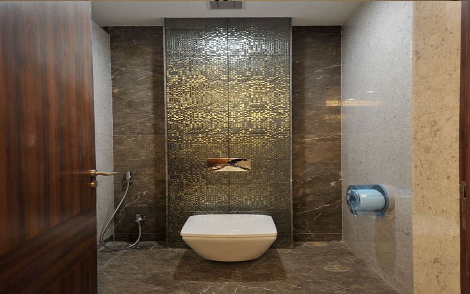 Washroom cubicle with a wall-hung WC against a gold glass mosaic panel between marble-clad walls