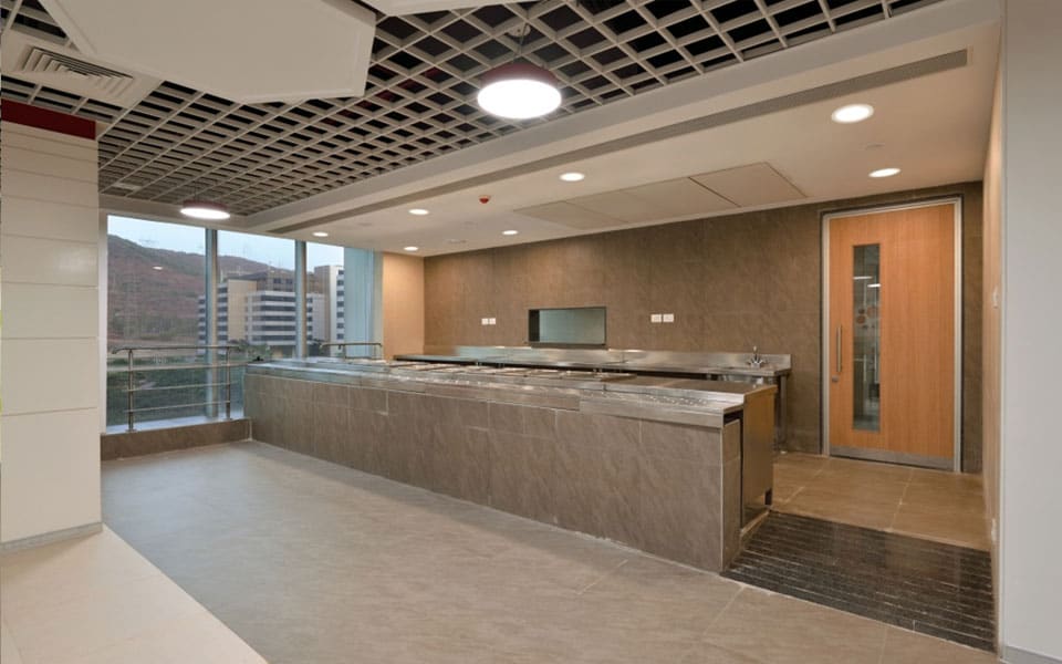 Cafeteria servery with a stone-clad counter, stainless bain-marie hot wells and glazing overlooking a hillside