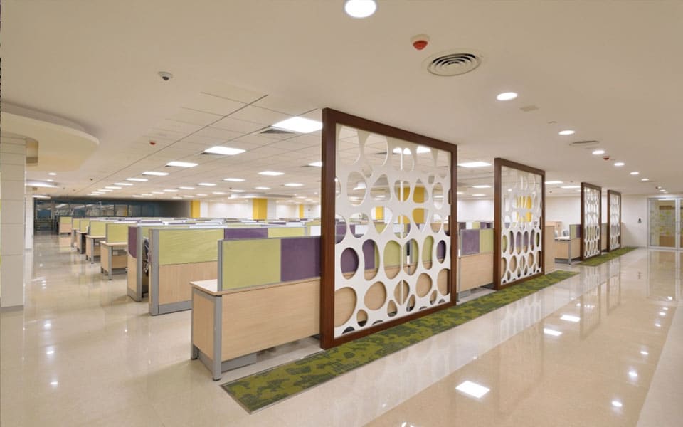 Circulation spine flanked by CNC-cut white jaali screens in timber frames beside green patterned carpet and workstations