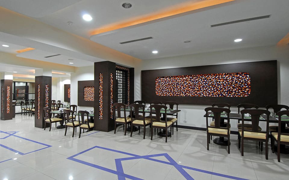 Dining hall with dark panelled columns, a backlit multicoloured mosaic inlay and glass-topped tables