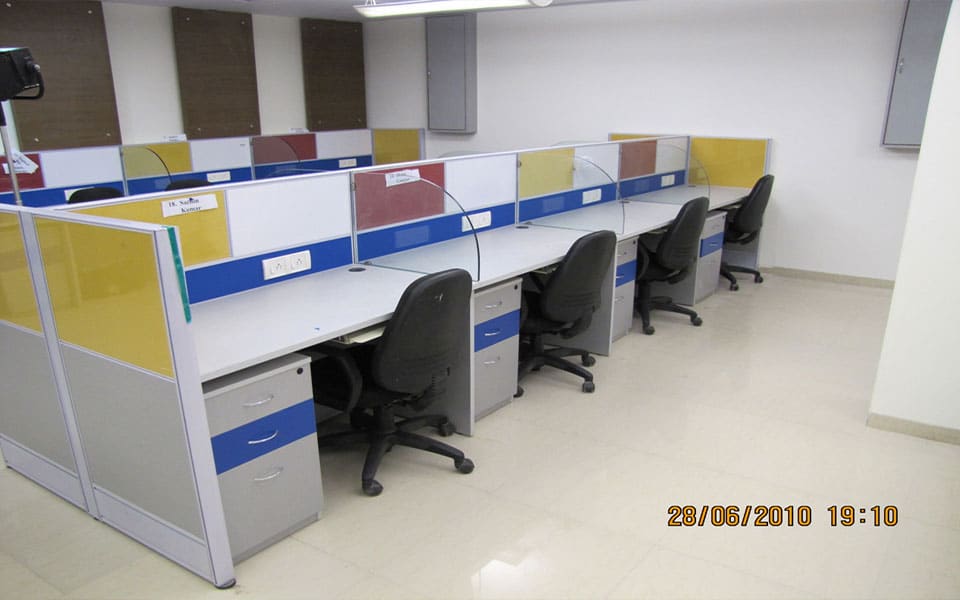 Empty open-plan bay with linear desking, yellow and blue partition screens and black task chairs