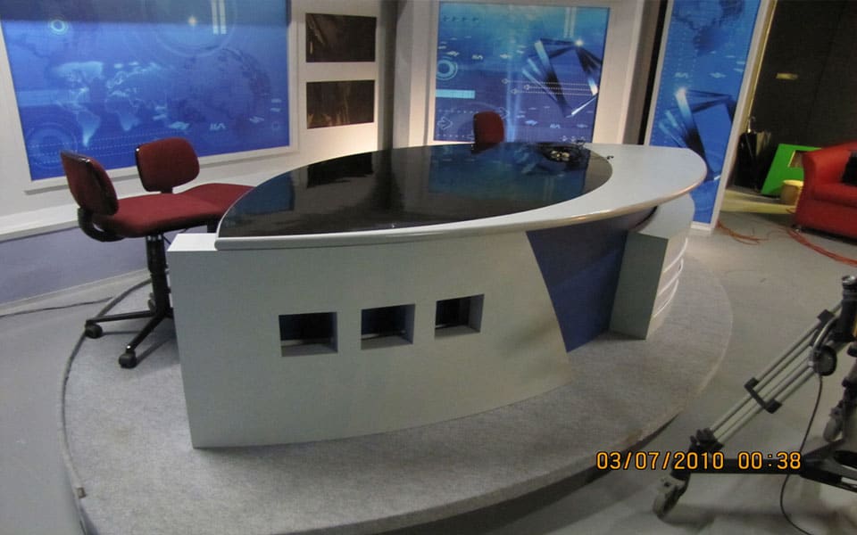 Television studio anchor desk with a gloss black top and curved fascia before backlit world-map panels